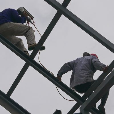 Two structural steel workers working on a high rooftop for a house roof structure installation